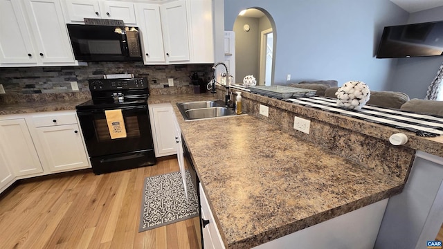 kitchen featuring light wood-style flooring, a peninsula, white cabinets, black appliances, and a sink