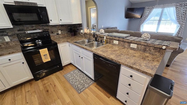 kitchen featuring a peninsula, arched walkways, a sink, black appliances, and light wood-style floors