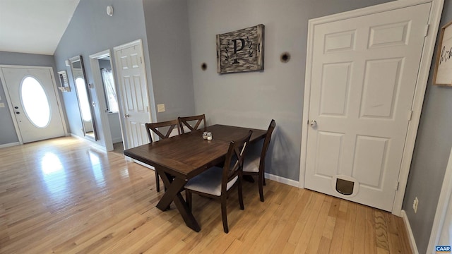 dining area featuring light wood-type flooring, baseboards, and vaulted ceiling