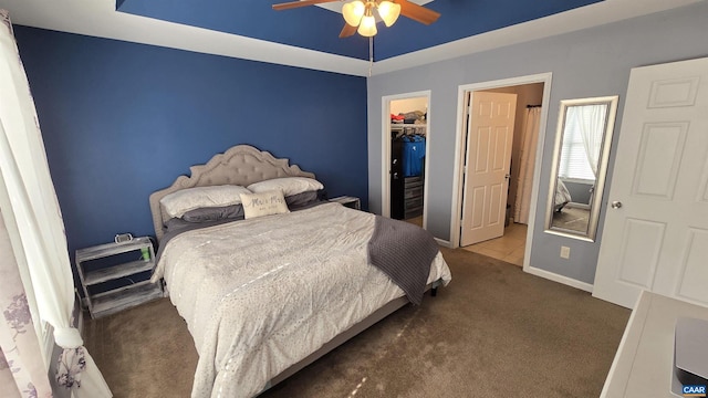 bedroom with a walk in closet, a tray ceiling, a closet, carpet flooring, and baseboards