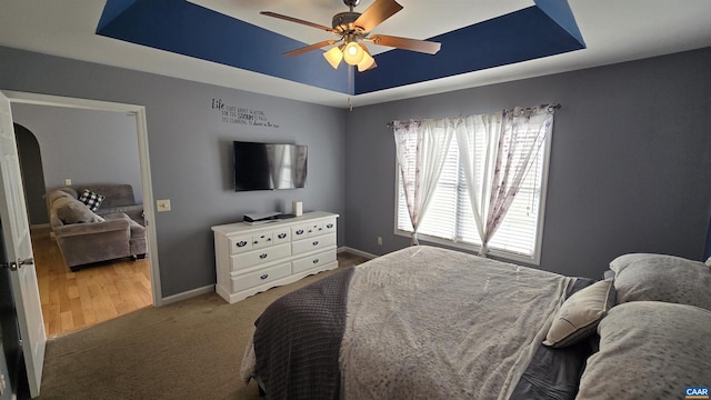 carpeted bedroom featuring a ceiling fan, a tray ceiling, baseboards, and arched walkways