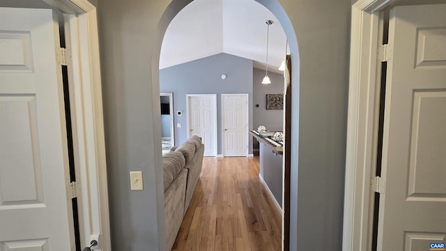 corridor featuring arched walkways, wood finished floors, and vaulted ceiling