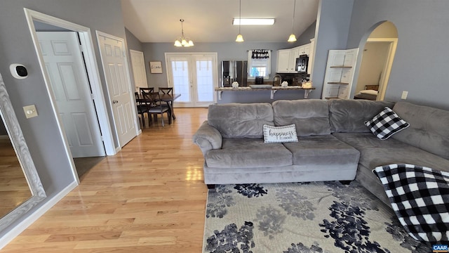 living room with baseboards, vaulted ceiling, light wood-style flooring, french doors, and arched walkways