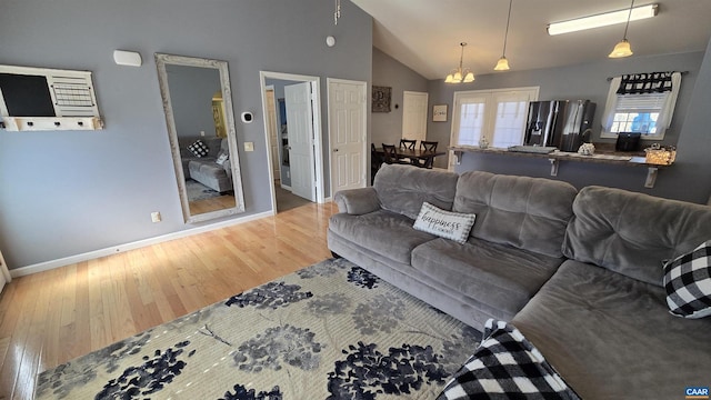 living room featuring vaulted ceiling, wood finished floors, baseboards, and french doors