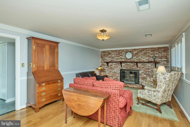 living room featuring a brick fireplace, visible vents, light wood finished floors, and ornamental molding