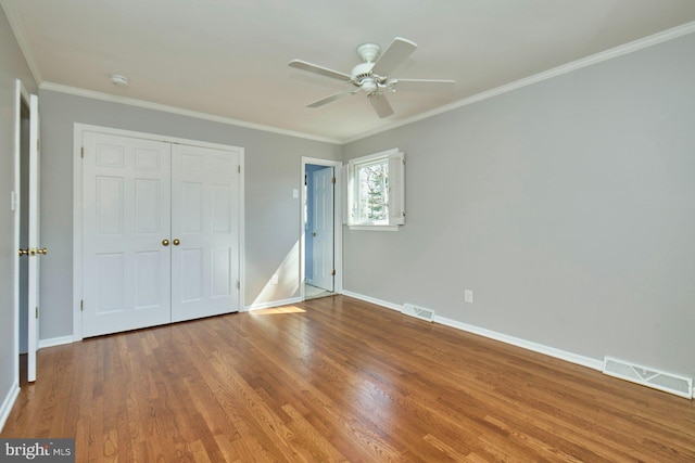 unfurnished bedroom with visible vents, baseboards, wood finished floors, and crown molding