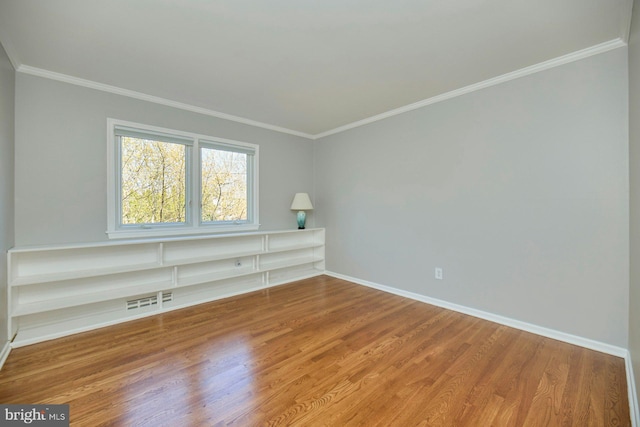 empty room featuring baseboards, wood finished floors, visible vents, and ornamental molding