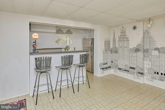 kitchen with brick patterned floor, a breakfast bar, and freestanding refrigerator