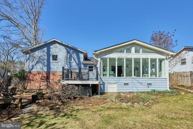 rear view of property featuring a deck, fence, a lawn, and a sunroom