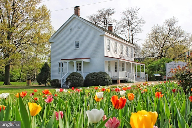 view of front of home featuring a porch, a chimney, and a front lawn