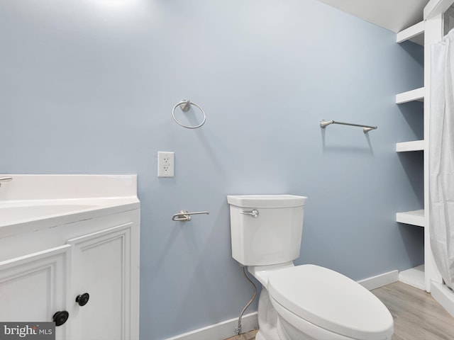 bathroom featuring baseboards, toilet, wood finished floors, and vanity