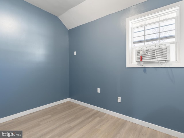 empty room featuring cooling unit, light wood-type flooring, baseboards, and vaulted ceiling