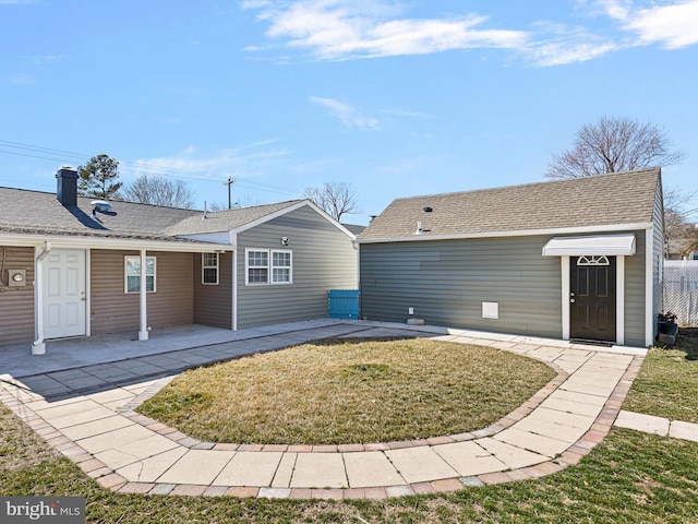 back of house featuring a patio, fence, a yard, an outdoor structure, and a shingled roof