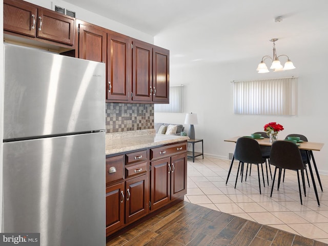 kitchen featuring pendant lighting, decorative backsplash, freestanding refrigerator, an inviting chandelier, and wood finished floors