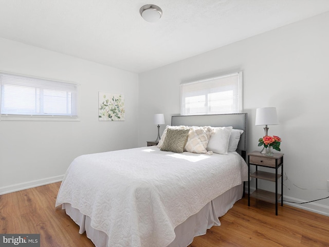 bedroom with multiple windows, wood finished floors, and baseboards