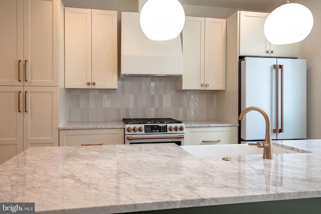 kitchen featuring a sink, backsplash, high quality appliances, and wall chimney range hood