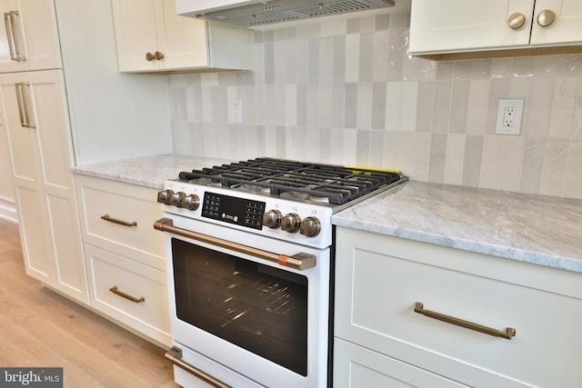 kitchen with light stone counters, wall chimney range hood, tasteful backsplash, light wood finished floors, and white gas range