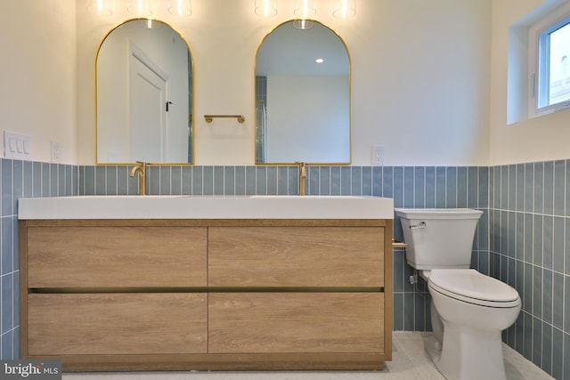 bathroom featuring wainscoting, toilet, tile walls, and double vanity