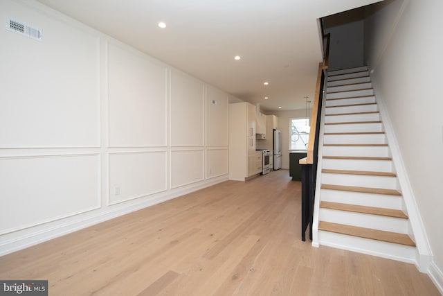 stairway featuring a decorative wall, recessed lighting, visible vents, and wood finished floors