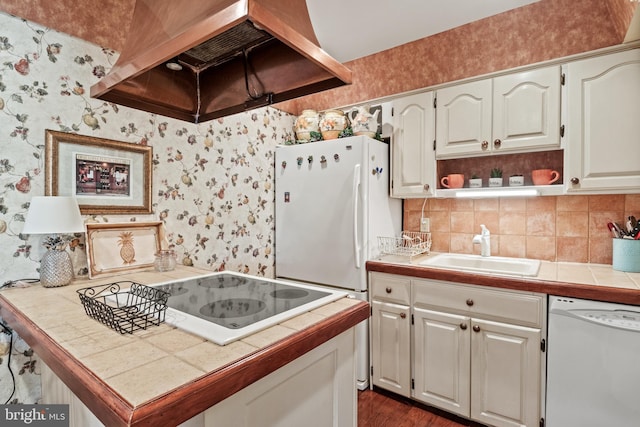 kitchen featuring a sink, tile countertops, white appliances, wall chimney exhaust hood, and wallpapered walls