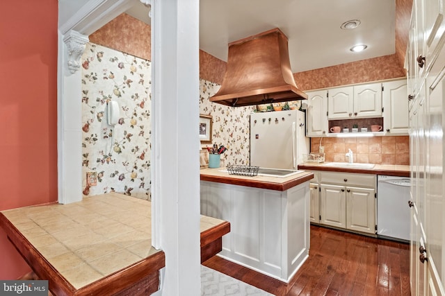 kitchen featuring island exhaust hood, a sink, white cabinetry, white appliances, and wallpapered walls