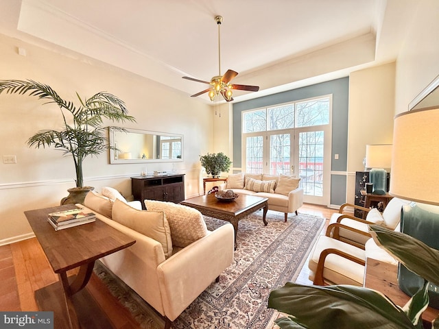 living area featuring a tray ceiling, baseboards, wood finished floors, and a ceiling fan