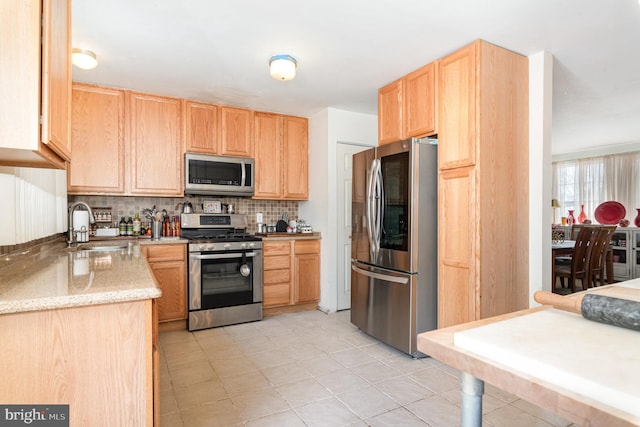 kitchen with light brown cabinetry, a sink, tasteful backsplash, appliances with stainless steel finishes, and light stone countertops