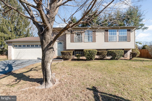 tri-level home with a front yard, fence, an attached garage, aphalt driveway, and brick siding