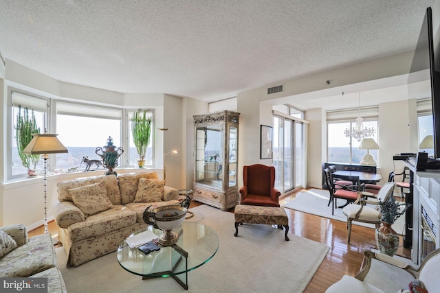 living room with visible vents, a notable chandelier, wood finished floors, and a textured ceiling