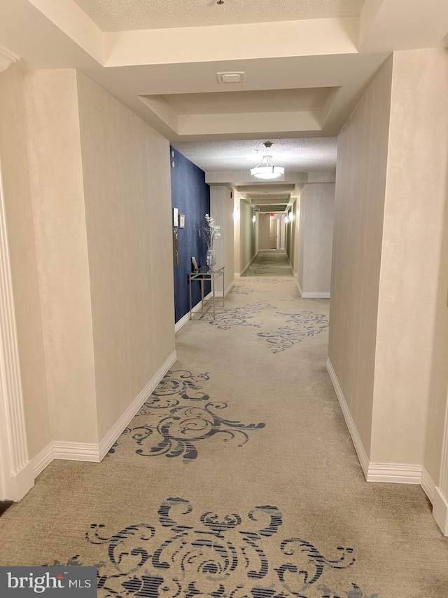 hall with visible vents, baseboards, light colored carpet, a textured ceiling, and a raised ceiling