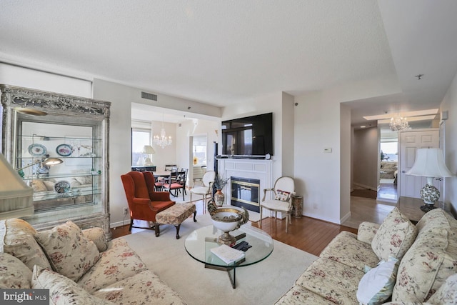 living room featuring visible vents, a glass covered fireplace, wood finished floors, a notable chandelier, and a textured ceiling