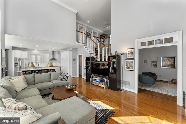 living area with baseboards, stairway, ornamental molding, a high ceiling, and wood finished floors