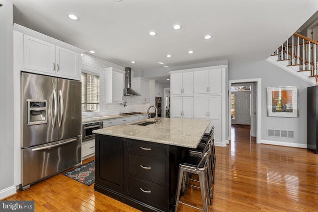 kitchen with visible vents, a sink, stainless steel appliances, white cabinetry, and wall chimney exhaust hood