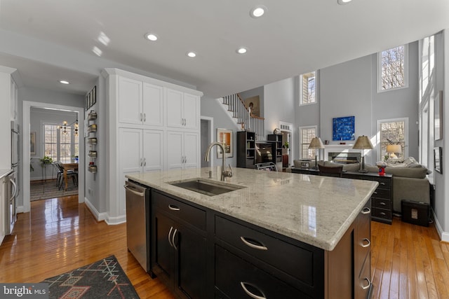 kitchen featuring dishwasher, light wood-type flooring, an island with sink, white cabinetry, and a sink