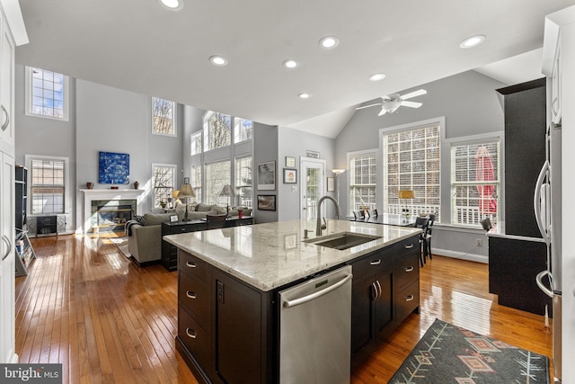 kitchen featuring a glass covered fireplace, dark wood finished floors, an island with sink, a sink, and stainless steel dishwasher