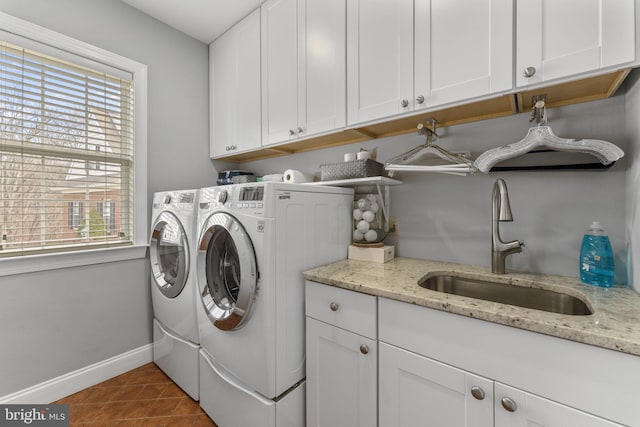 clothes washing area with tile patterned floors, a sink, washing machine and dryer, cabinet space, and baseboards