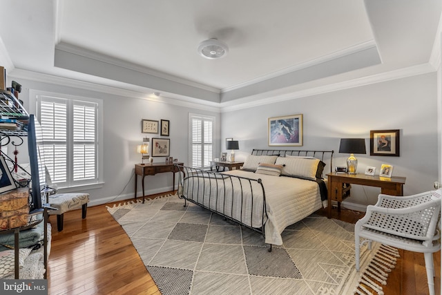 bedroom featuring baseboards, a raised ceiling, light wood-style floors, and ornamental molding