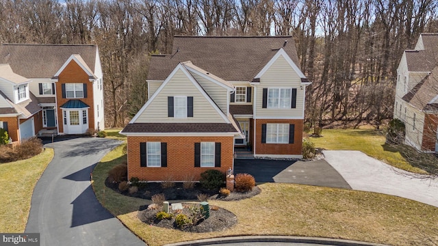 traditional-style home featuring a front yard, brick siding, roof with shingles, and driveway