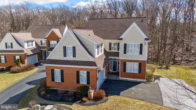 traditional home featuring brick siding, driveway, and a shingled roof