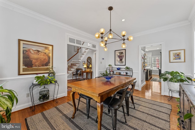 dining room featuring baseboards, light wood-style floors, ornamental molding, and stairs