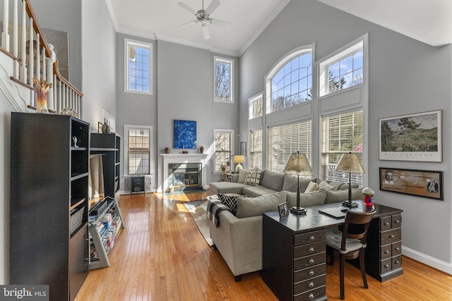 living area featuring ceiling fan, baseboards, a fireplace with flush hearth, light wood-type flooring, and ornamental molding