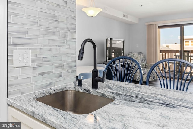 kitchen featuring light stone counters, visible vents, white cabinets, and a sink