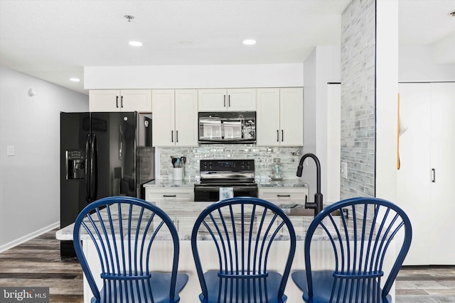 kitchen with decorative backsplash, white cabinetry, black appliances, and wood finished floors