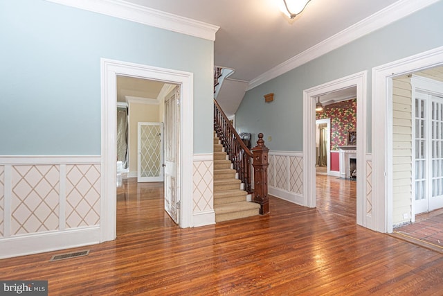 foyer entrance featuring wood finished floors, visible vents, a wainscoted wall, ornamental molding, and stairs