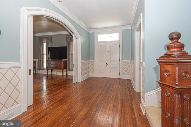 entryway featuring arched walkways, wood finished floors, wainscoting, and ornamental molding