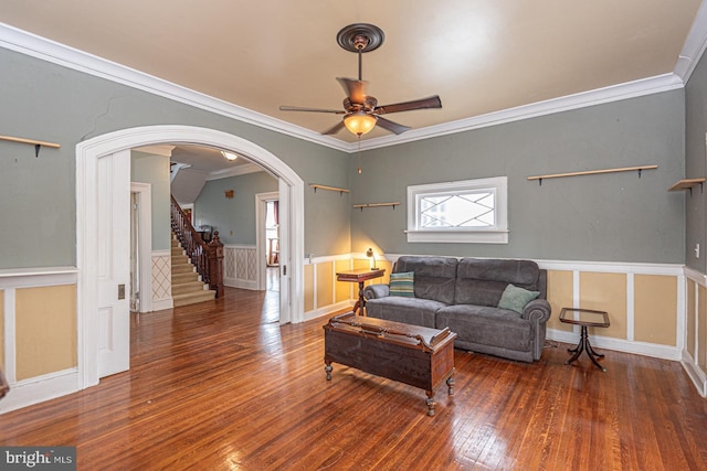 living area with crown molding, a wainscoted wall, stairs, arched walkways, and wood-type flooring