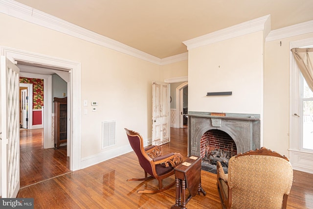 living area with wood finished floors, baseboards, visible vents, a fireplace with flush hearth, and ornamental molding