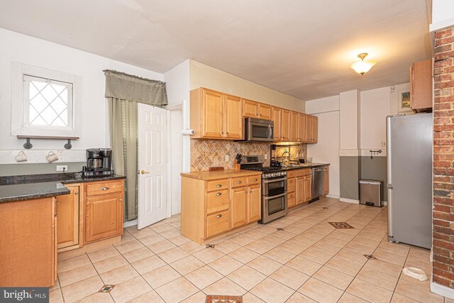 kitchen with decorative backsplash, dark countertops, light tile patterned floors, and stainless steel appliances