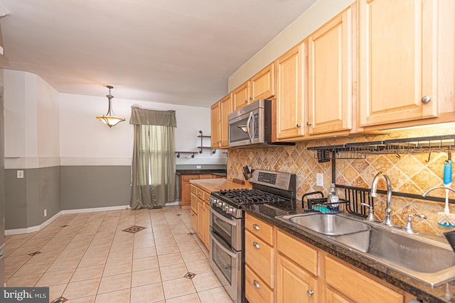 kitchen featuring dark countertops, light brown cabinetry, appliances with stainless steel finishes, light tile patterned flooring, and a sink