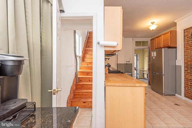 kitchen featuring light tile patterned floors, brick wall, and freestanding refrigerator